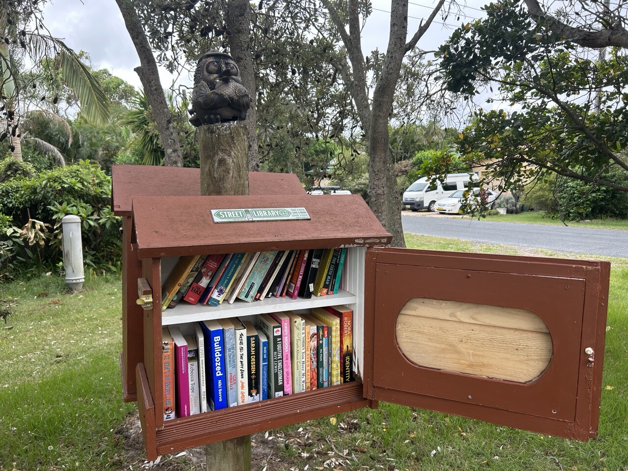 A little Street, Library, a sort of nesting box filled with literature, made out of timber resembling a cottage of some sort in a long foot part in suburbia