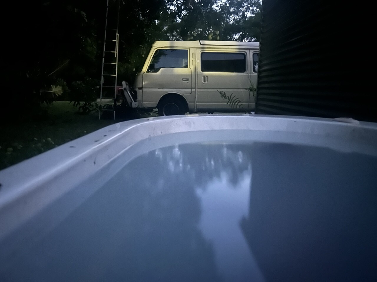 Roly’s  bath tub in the garden in the outdoors filled to the brim with  water as hot as I can tolerate.  In the background is 1983 Nissan Urvan, carefully position so the neighbours don’t have to watch me bath from about 150 yards away.
